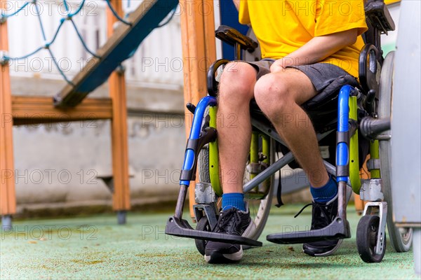 Detail of a disabled person in a wheelchair on the swings of a playground