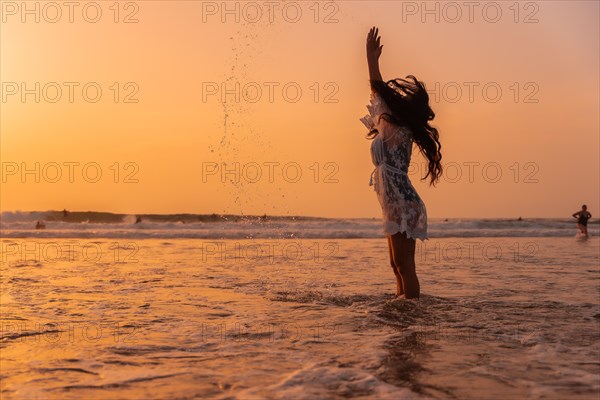 A woman in the sunset in a white dress in the sea in summer throwing water on vacation