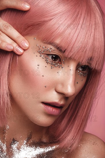 Beautiful woman in a pink wig and creative makeup with rhinestones. Beauty face. Photo taken in the studio