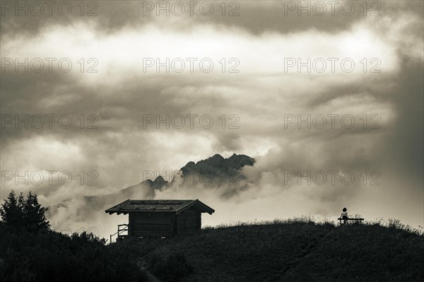 Mountain hut with bench and climber and dramatic clouds in the background