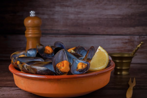 Steamed mussels with lemon in clay pot with metal mortar and pepper shaker