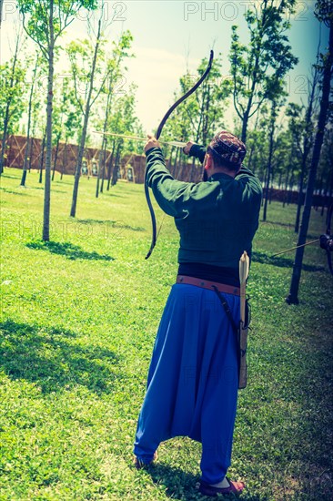 Archer with bow in traditional clothes shooting an arrow