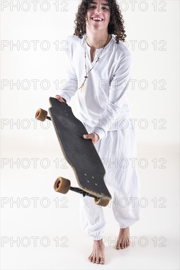 Front view of a young man with curly hair wearing white clothes and walking while holding a skate over white background