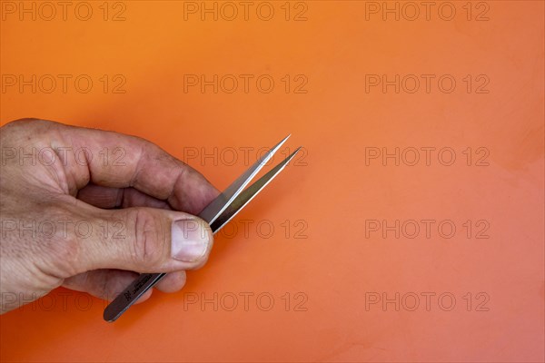 Male hand holding a pair of medical tweezers against an orange background