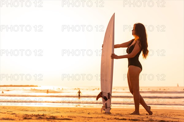 Portrait of a surfer woman on a beach at sunset with the surfboard