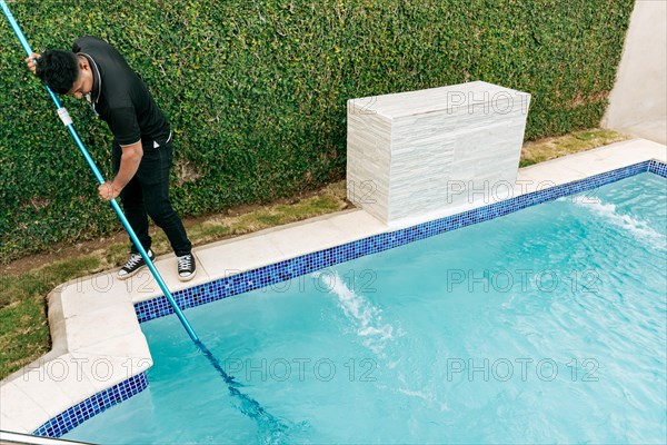 Maintenance person cleaning a swimming pool with skimmer