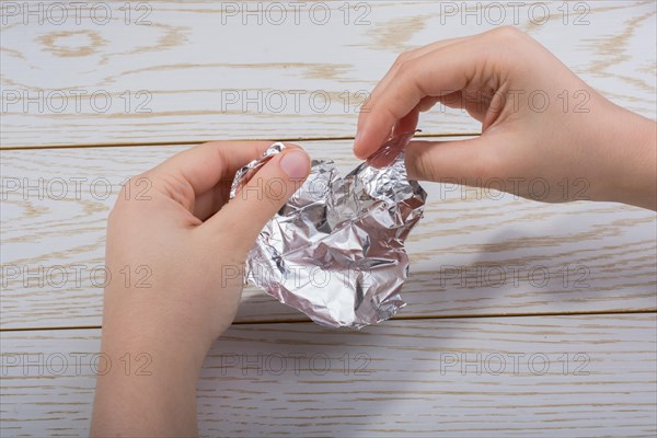 Hand tearing a heart shaped aluminium foil on a wooden background