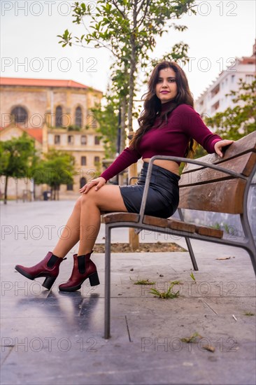 A brunette woman in a leather skirt sitting in the city with a church in the background in autumn