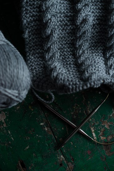 Grey knitted piece with knitting pattern and knitting needles