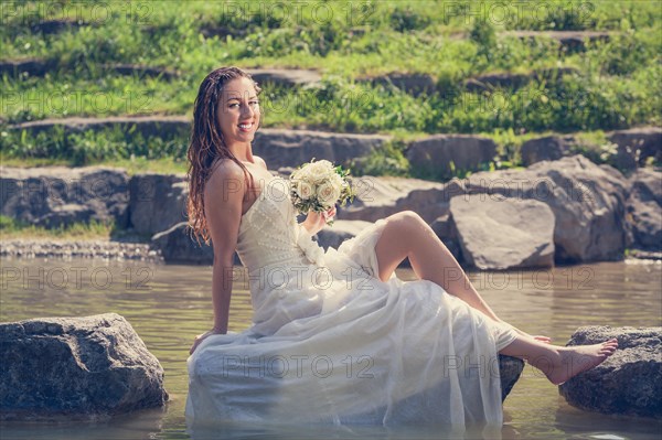 Bride in wet dress sits on a stone