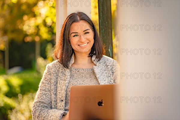 Pretty woman with glasses and MacBook in hand sits in the park at autumn time