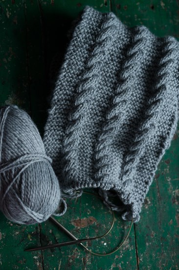 Grey knitted piece with knitting pattern and knitting needles