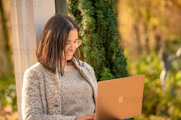 Pretty woman with glasses and MacBook in hand sits in the park at autumn time