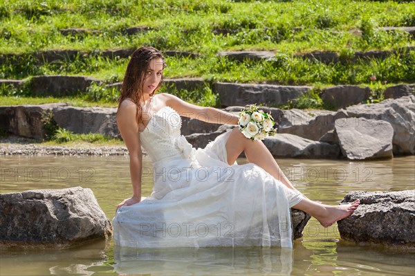 Bride in wet dress sits on a stone