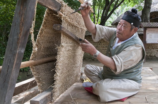 Man weaving a straw floor mat with a traditional loom