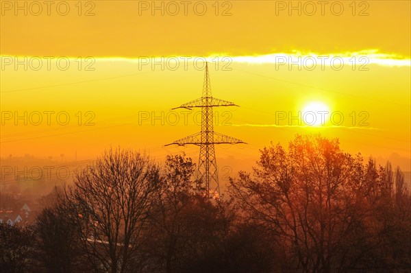 Backlight shot of a sunrise in front of an overhead power line mast in Bavaria