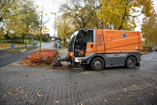 Sweeper sweeps leaves in autumn