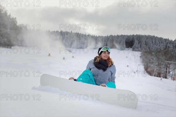 Woman with snowboard sitting in the snow