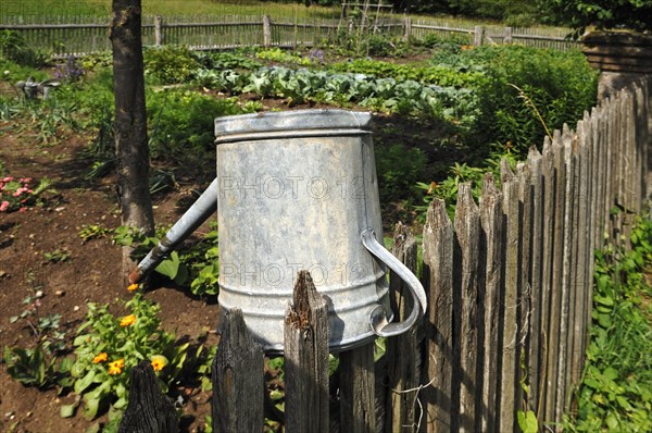 Watering can on a wooden fence near the farm garden