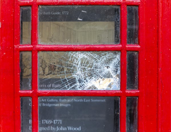 Smashed vandalised glass panel of old red telephone box