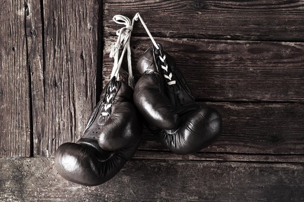 Old leather boxing gloves hanging in front of rustic wooden wall