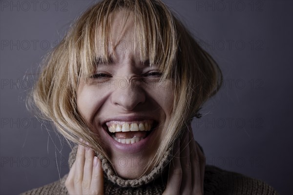 Young woman with turtleneck jumper and long hair laughs into camera