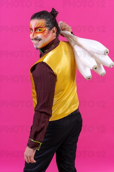 Portrait of a juggler in a waistcoat and with painted face juggling maces on a pink background