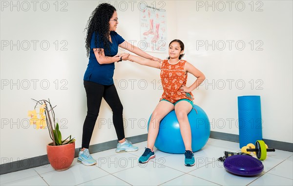 Physiotherapist assisting female patient sitting on rehabilitation ball. Rehabilitation therapy with fitness ball