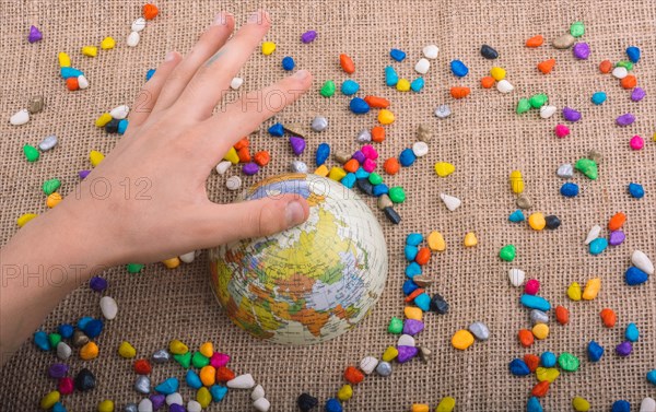 Hand holding globe placed amid colorful pebbles