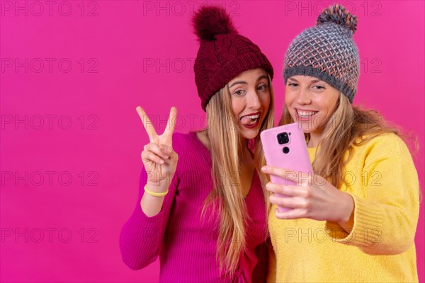 Two young blonde caucasian women with a phone isolated on a pink background