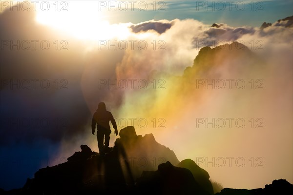 A climber walking along a ridge during a sunrise in the clouds