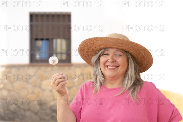 Woman with hat and white hair smiling with a dandelion in her hand