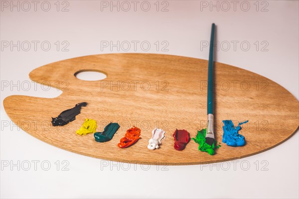 Wooden palette with colored oil paints and brushes isolated on a white background