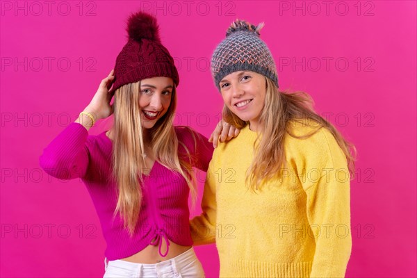 Two blonde caucasian women in wool hats on a pink background