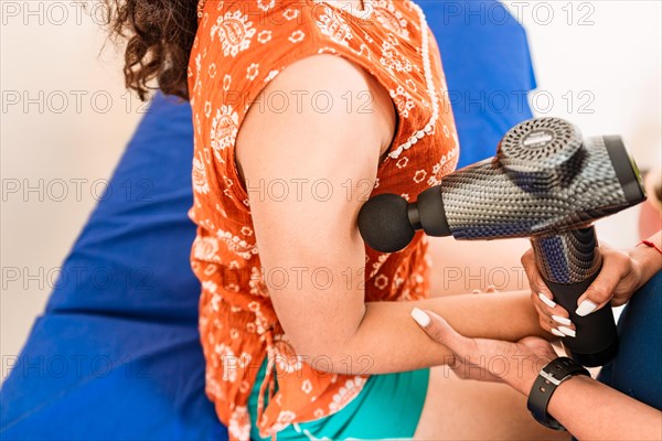 Closeup of physiotherapist using massage gun on female patient. Chiropractor using massage gun on patient arm