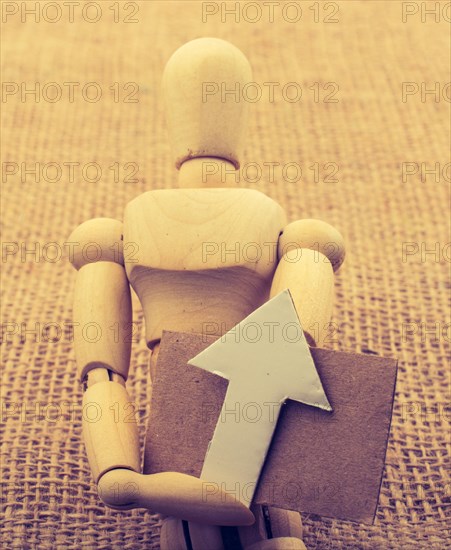 Wooden man holding a paper arrow on canvas
