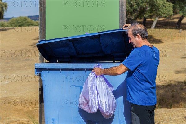 Man throwing garbage bags into a dumpster with a blank sign for copy space