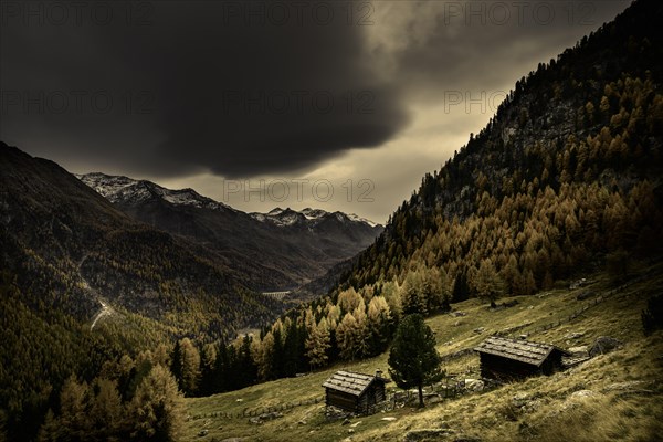 Mountain hut on mountain meadow with autumnal mountain forest and threatening cloudy sky