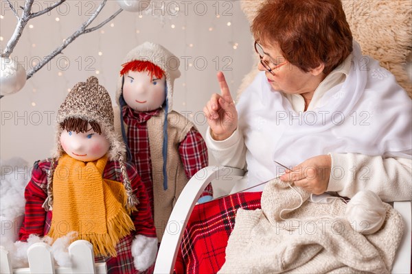 A nice elderly woman sews to knit her granddaughters in a Christmas arrangement. In studio