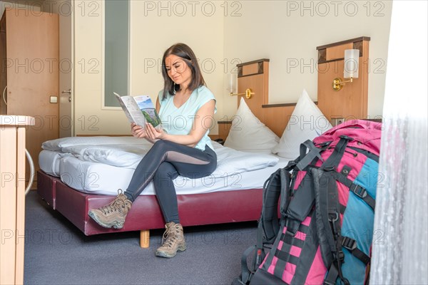 Attractive hiking woman sitting on a hotel bed looking at the hiking map