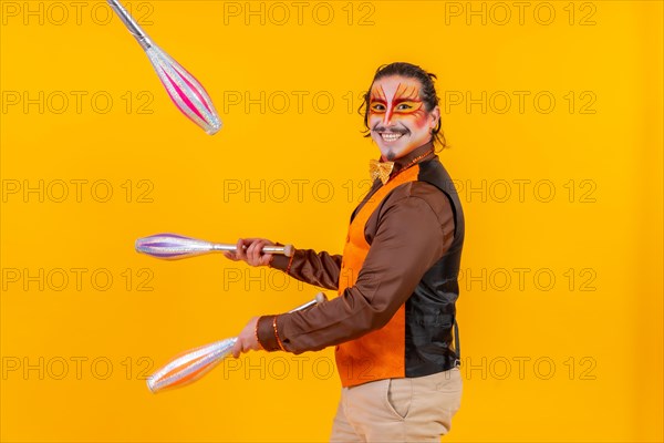 Juggler in a vest with makeup juggling with maces on a yellow background