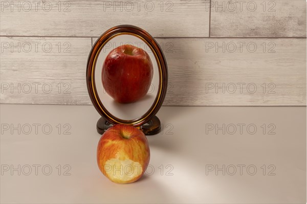 Bitten red apple reflected in a mirror isolated on a white table with copy space