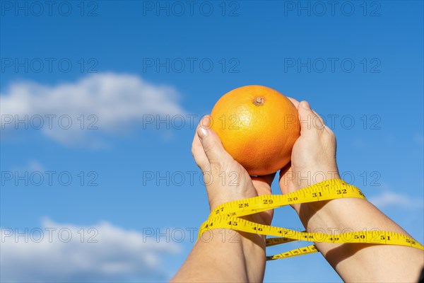 Woman holding a grapefruit in her hands with a tape measure and a sky with clouds in the background