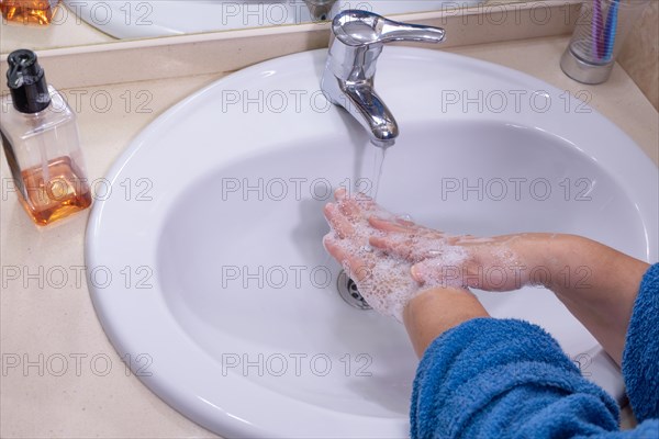 Woman in blue bathrobe washing her hands in her bathroom