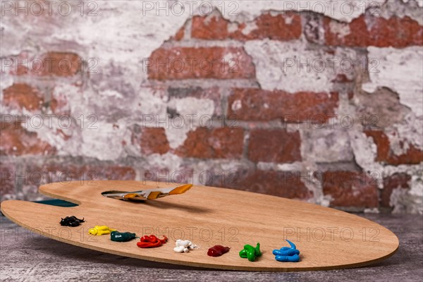 Wooden palette with colored oil paint and brushes with a brick wall in the background