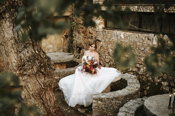 Beautiful bride with her bouquet sititng in the stone garden