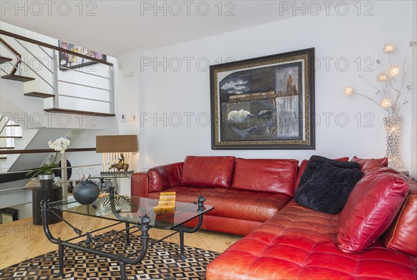 Red leather sectional sofa and black wrought iron with glass top coffee table in living room inside modern home