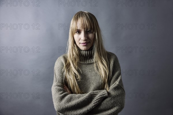 Woman with long blond hair and warm woollen jumper crosses her arms