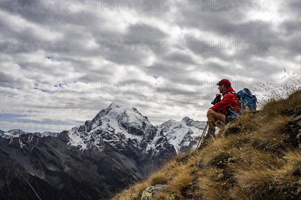 Mountaineer on autumnal mountain meadow with cloudy sky in front of Ortler summit massif