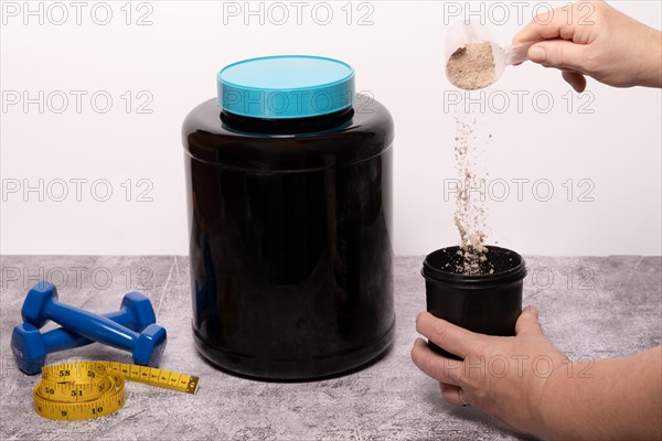 Woman pouring a scoop of protein powder in an insulated shaker on a black background